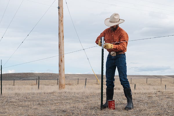 Ranch putting a barbed wire fencing line on a t-post. 