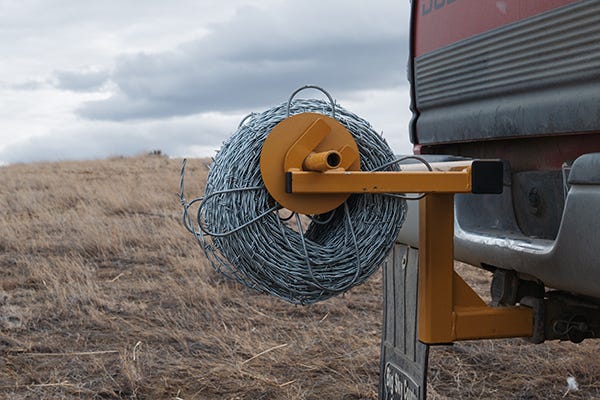 Roll of barbed wire on Tarter unwinder on the back of a pick up. 