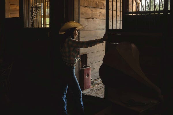 Girl in straw hat closing gate in barn with western shirt on and blue jeans with record player in foreground