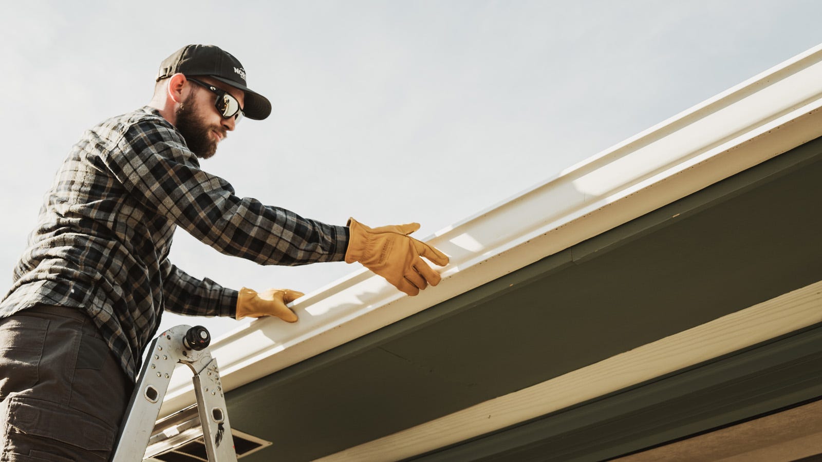 A man cleans out his gutters while standing on a ladder