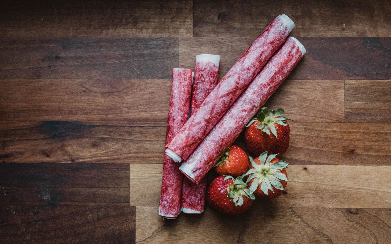Four homemade strawberry fruit leather rolls next to fresh strawberries on a butcherblock
