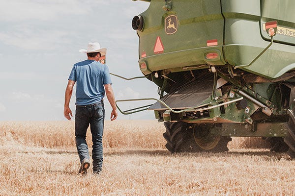 A man in a cowboy hat walking toward a John Deere combine combine in a wheat field