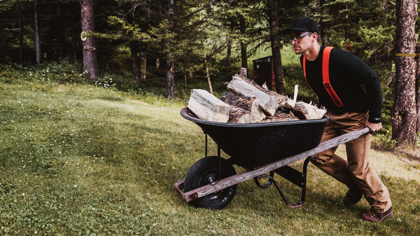 A man pushing a wheelbarrow with wood up a hill