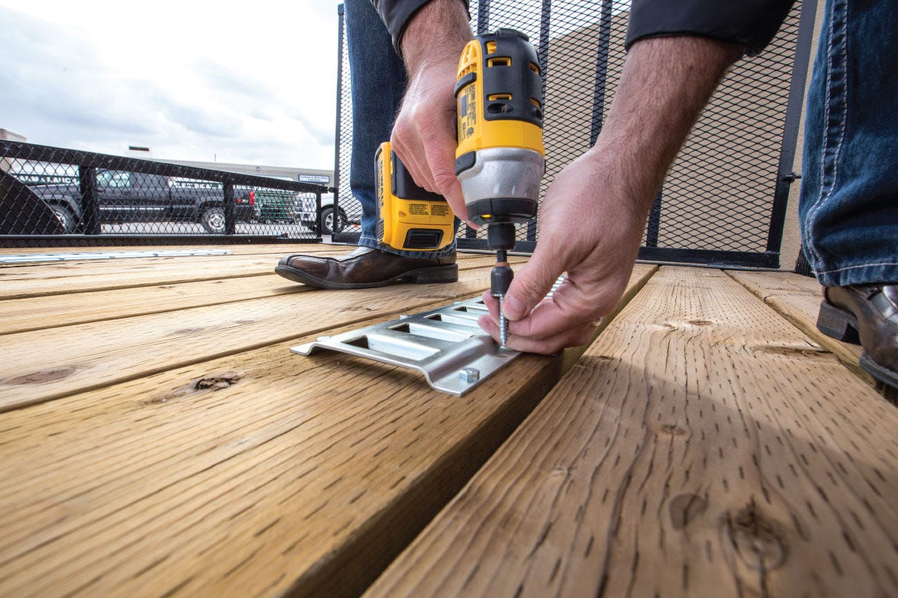 A man uses an electric DeWalt drill to secure a bracket to a wooden trailer