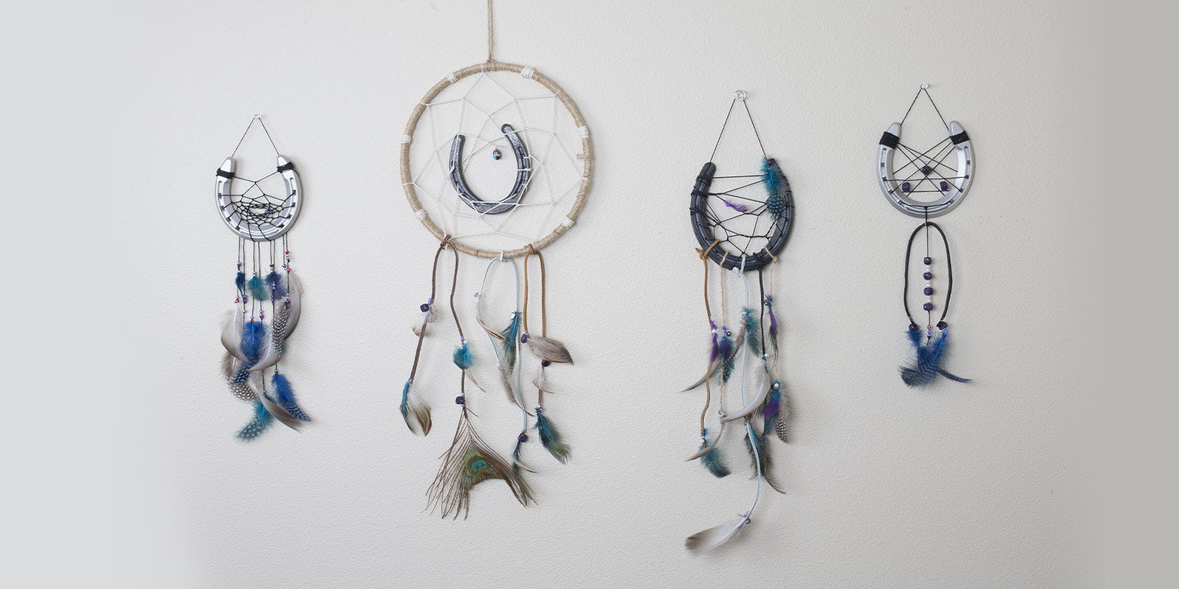Four different horseshoe dreamcatchers hang on a white wall