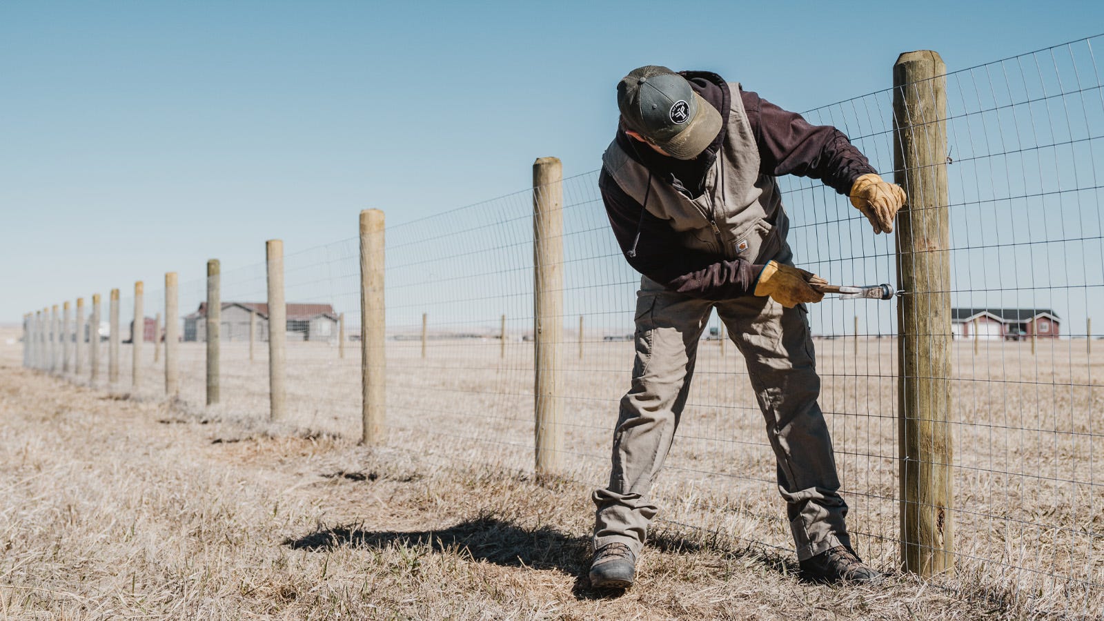 A man uses a hammer to pound in a staple to a new fence