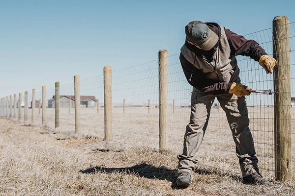 A man uses a hammer to pound in a staple to a new fence