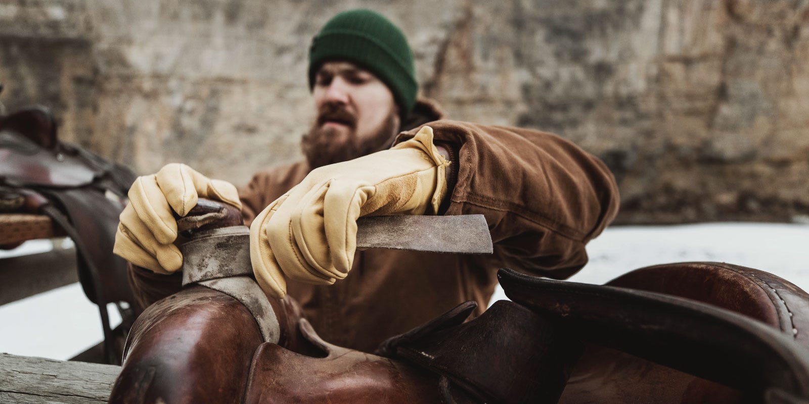 A man loads a saddle on a horse while wearing Noble Outfitters leather work gloves.