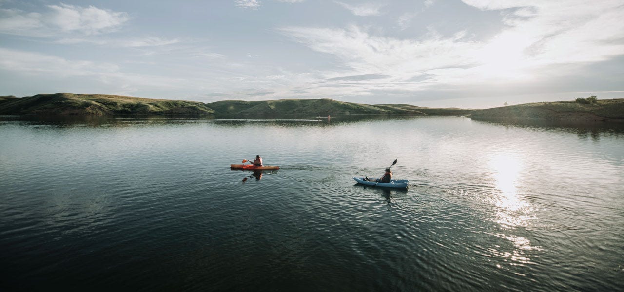 Two kayakers travel over an expansive Montana lake as the sun begins to set