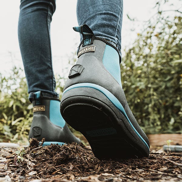 Six inch blue and black MUDS boots walking in a muddy forest.  Click to shop Noble MUDS six inch boots