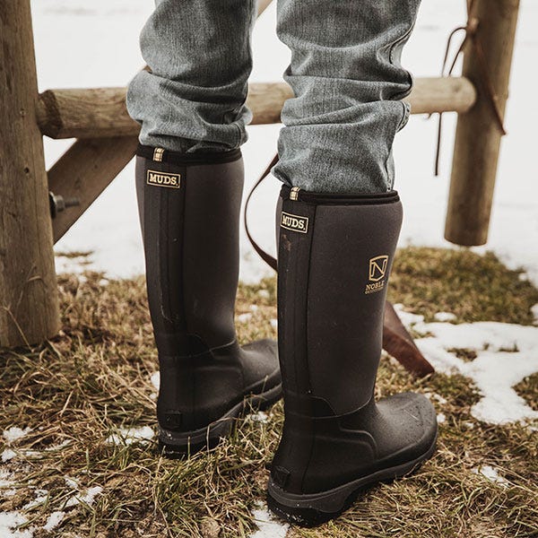 Noble MUDS high boots standing in a snow and grass covered farm
