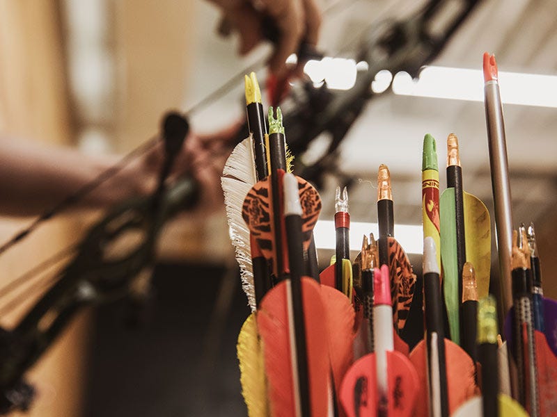 Arrow fletching in foreground with a bow being tuned in the background