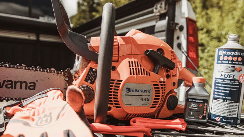 A Husquevarna chainsaw wits on a truck bed next to small bottle of chainsaw oil and fuel