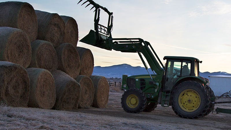 A John Deer tractor stacks hay bails with Montana mountains in the background