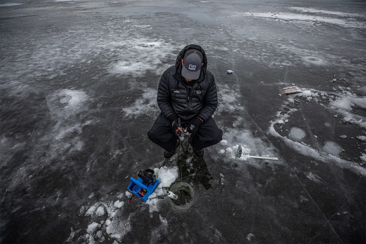 A single ice fisherman sits above a hole in the ice holding a rod