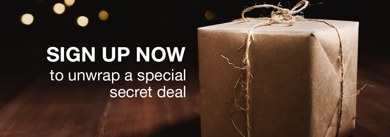 sign up now to unwrap a special secret deal. gift wrapped in front of tree.