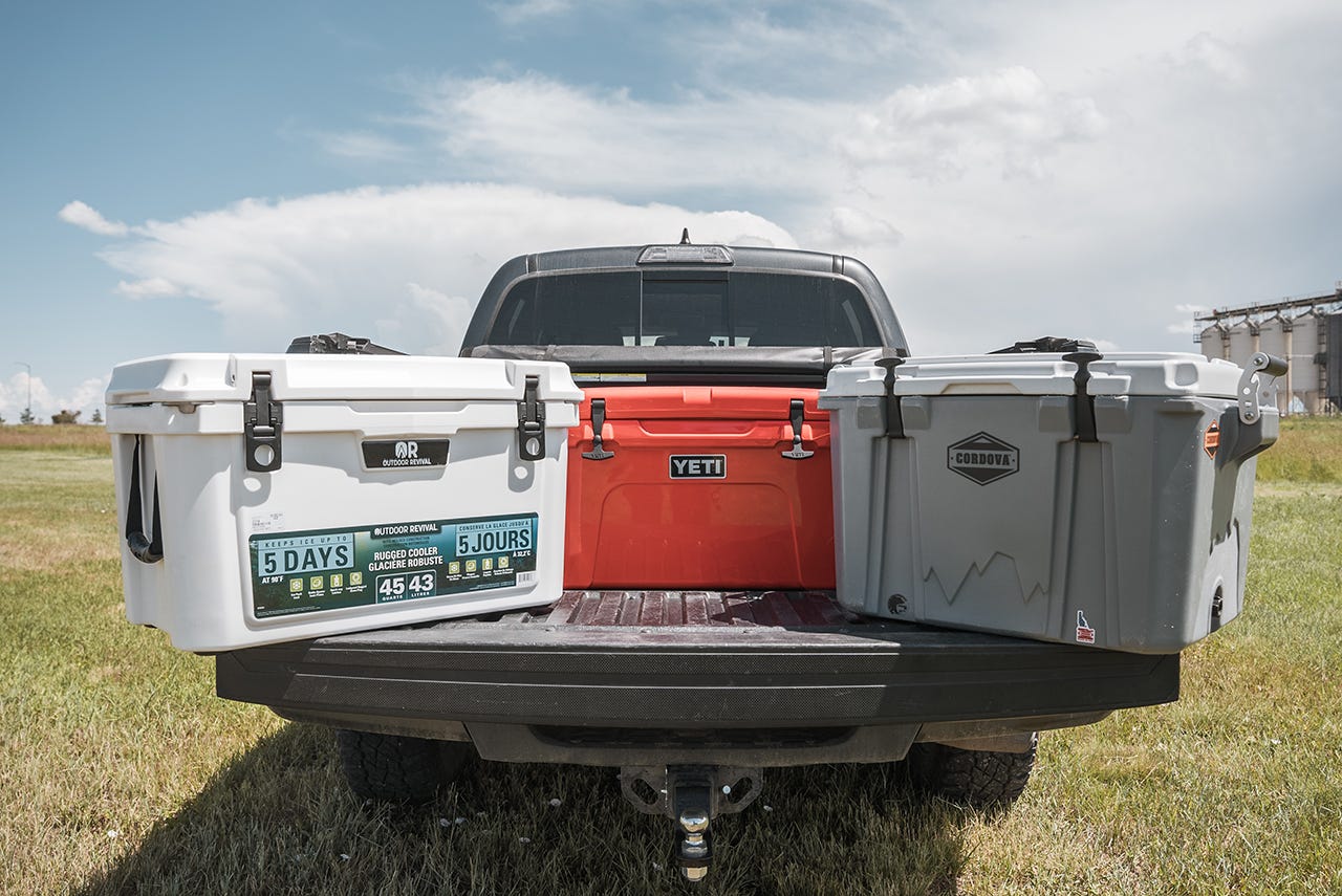 Three coolers, an Outdoor Revival, a Yeti, and a Cordova, sit in the back of a pickup.