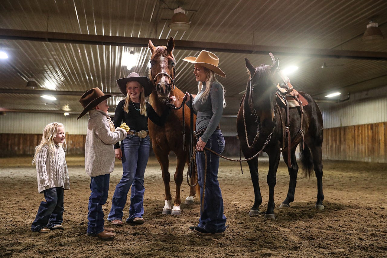 Lindsay Kruse talking to her three kids while standing with her horses in their barn near Fromberg, Montana