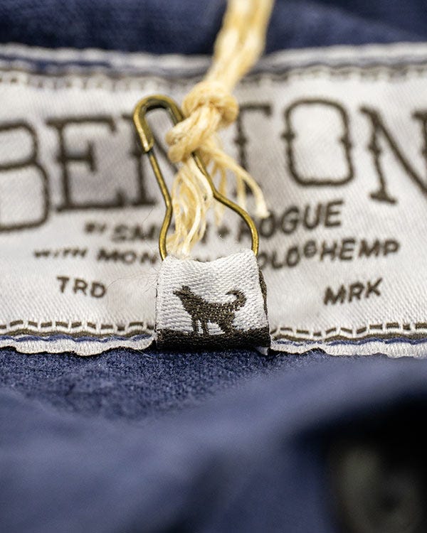 Close-up of the inside Benton shirt label attached to dark blue hemp fabric, featuring a small woven tag with a dog silhouette and hanging string fastener.