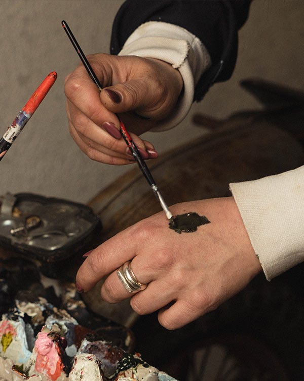 Close up of paintbrush painting the top of a hand, paint is on the table below