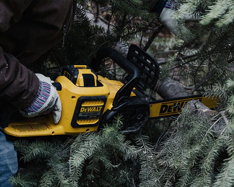 A DeWalt chainsaw being held with a man wearing Smith and Rogue gloves cuts down a Christmas tree