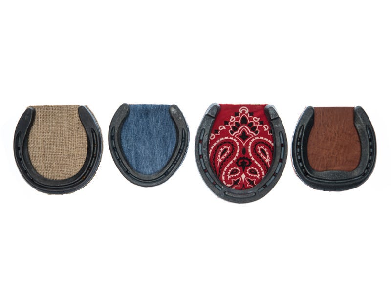 Four finished horseshoe coasters displayed side by side, each made with a metal horseshoe and a different fabric insert, including burlap, denim, red bandana, and leather.