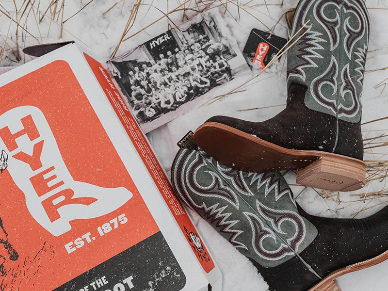  A pair of embroidered cowboy boots lying on snow beside a boot box and printed photographs.