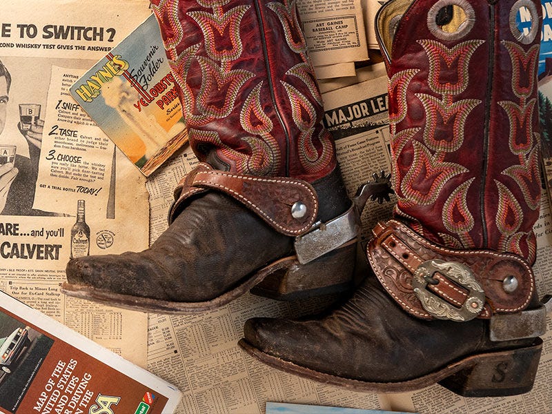 HYER cowboy boots, clearly used, laying across old newspaper with spurs on them.