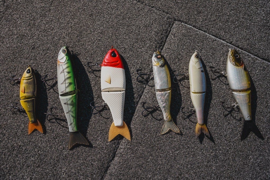 six different brands of glide baits laying on the deck of the boat, throwback baits, storm arashi, river2sea, 6th sense fishing draw, strike king hogfather
