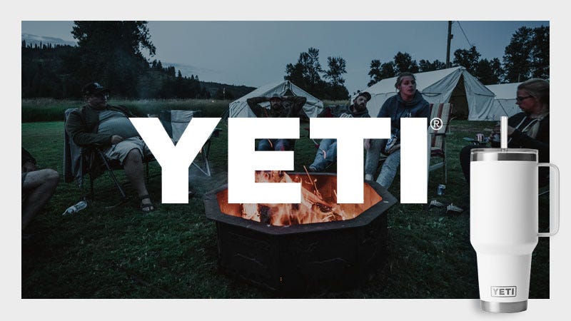 A group of people sit around a fire pit outdoors with tents in the background at dusk, partially covered by large white text reading "YETI." In the foreground on the right, a white YETI tumbler with a straw is displayed.