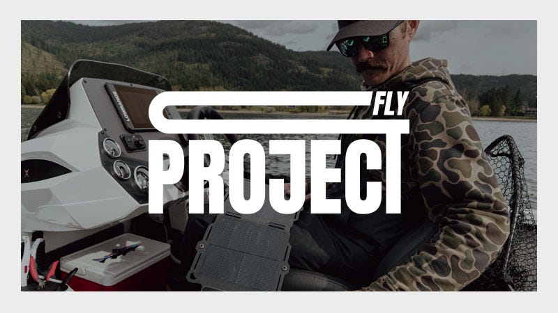 A man wearing a camouflage hoodie and sunglasses sits in a boat on a lake with forested hills in the background. The words "FLY PROJECT" are prominently overlaid across the image in large white text.