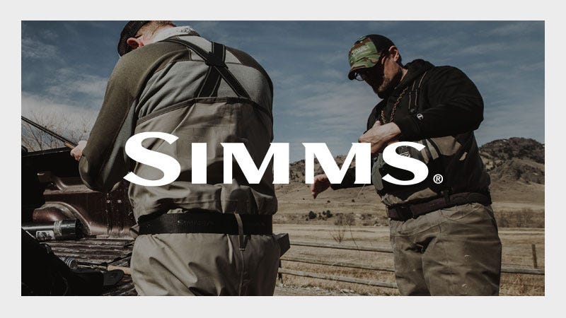 Two people wearing fishing waders and outdoor gear stand beside a pickup truck in a rural landscape; the word "SIMMS" is prominently displayed across the center of the image.