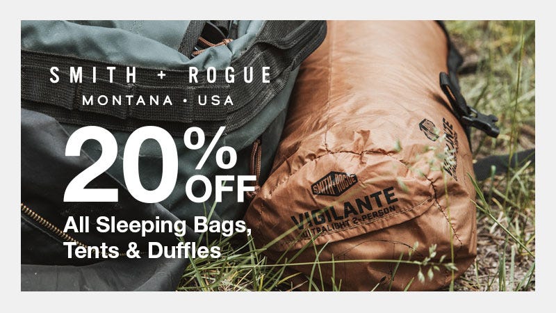 Close-up of a Smith & Rogue backpack and a rolled-up Vigilante 2-person sleeping bag lying in grass. Text on image reads: "Smith + Rogue, Montana • USA, 20% Off All Sleeping Bags, Tents & Duffles."