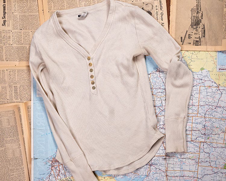 Smith + Rogue light-colored long-sleeve henley shirt with button placket, laid on vintage newspaper pages over a map background.