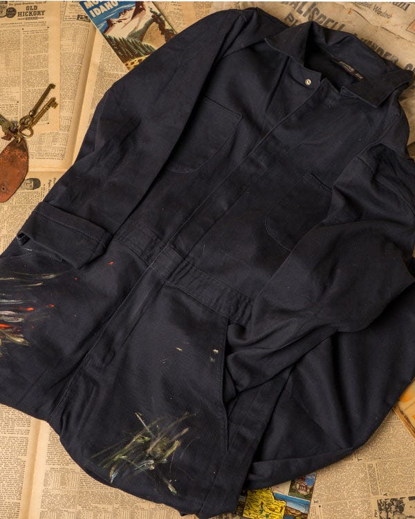 Berne dark work coveralls with paint marks laid on vintage newspaper pages with small tools and postcards.