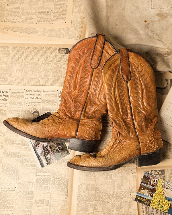 Pair of Dan Post brown leather cowboy boots with stitched detailing, placed on vintage newspaper pages beside a light-colored fabric.