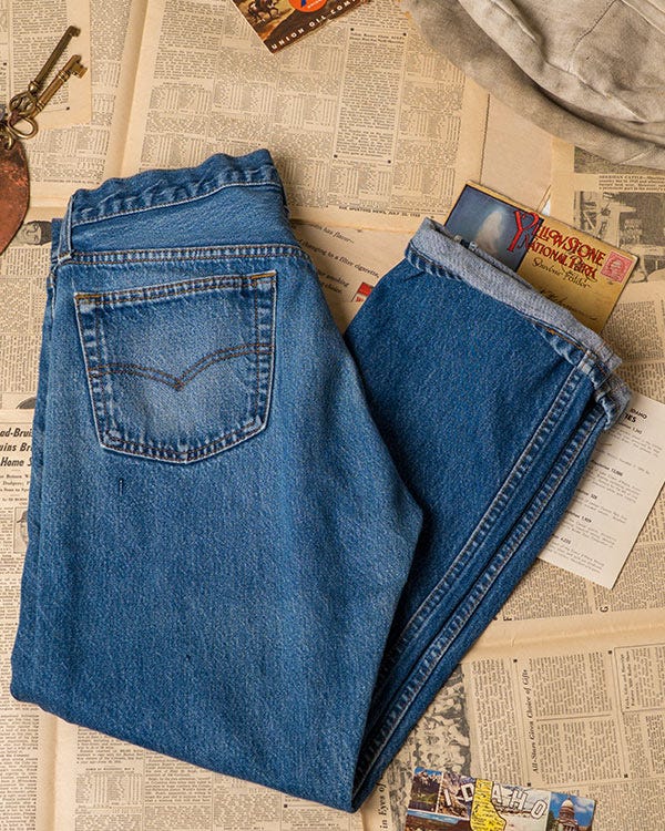 Levi&rsquo;s blue denim jeans folded to show the back pocket, laid on vintage newspaper pages with postcards.