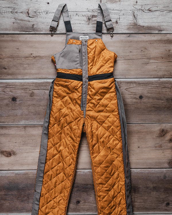 Smith + Rogue Original canvas bib overalls turned inside out, revealing full quilted insulation from top to bottom against a wooden background.