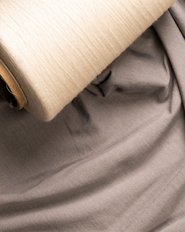 Close-up of soft gray Smith + Rogue Pima cotton tee fabric with a spool of matching Pima cotton thread, highlighting smooth texture and premium material quality.