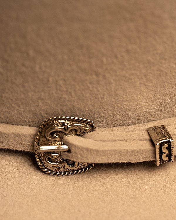 Close-up view of a tan felt cowboy hat band with a small decorative metal buckle attached.