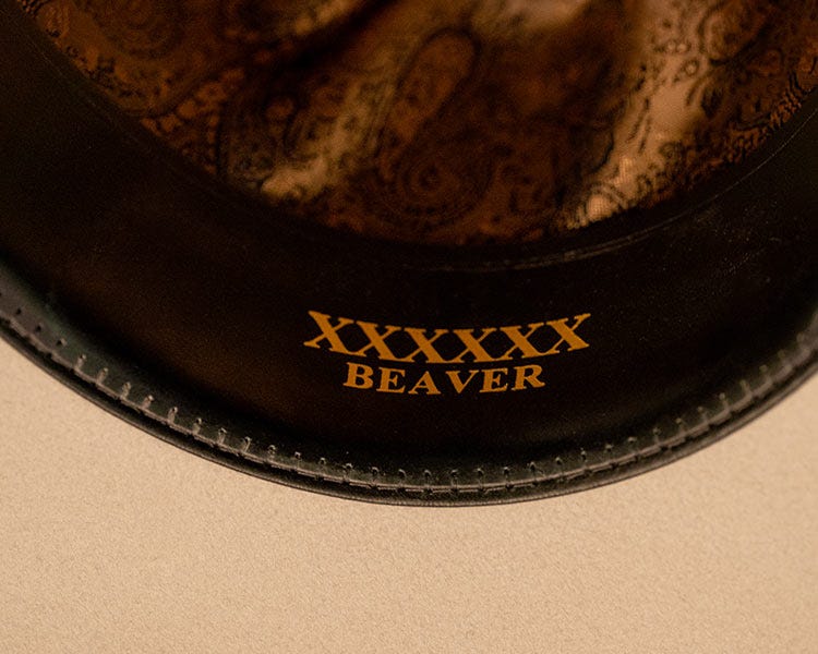 Close-up of the inside brim of a cowboy hat with gold lettering reading &lsquo;XXXXX BEAVER&rsquo; on the black leather edge.