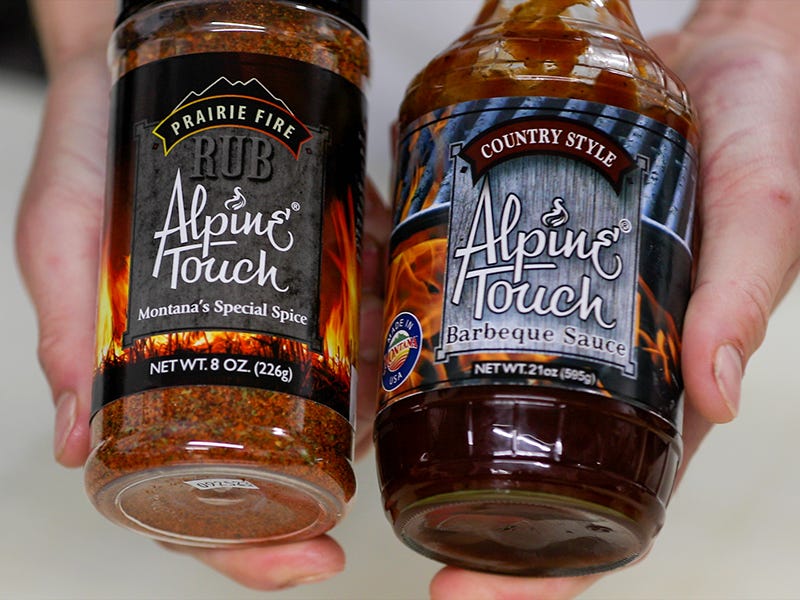 A man holding Alpine Touch rub and Alpine Touch BBQ next to each other