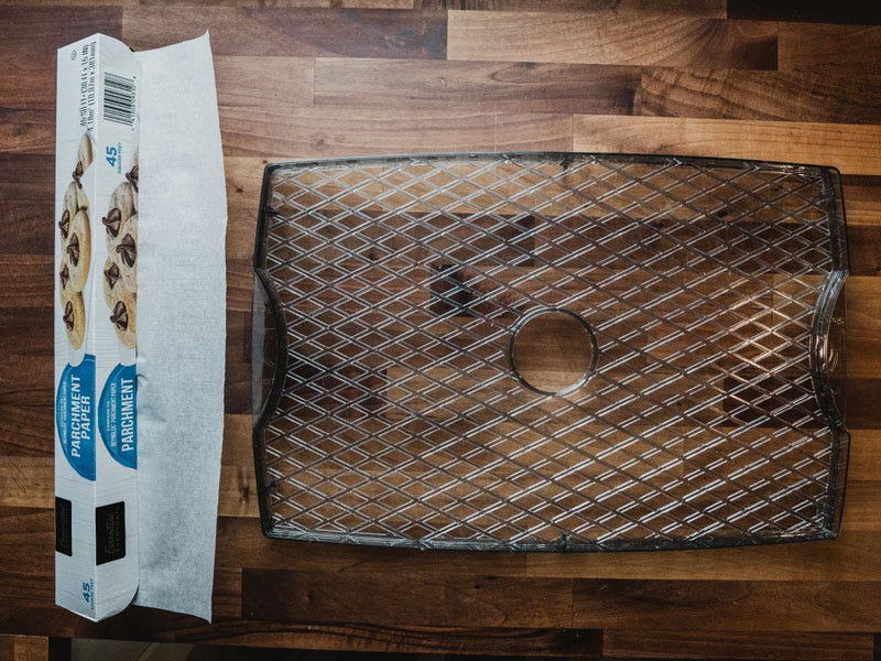 A roll of parchment paper sits next to a Craftworx dehydrator tray on a clean butcher block