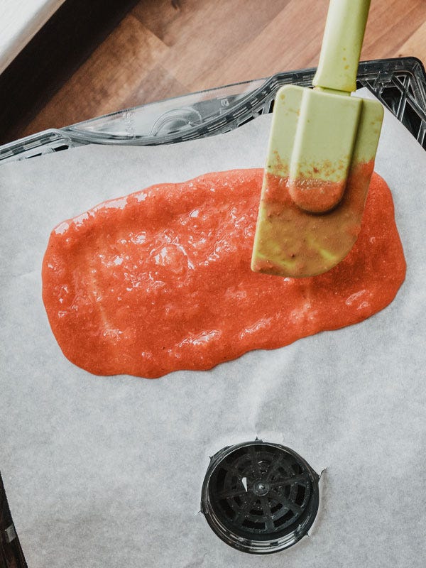 Spreading the fruit leather mixture on parchment paper using a rubber spatula