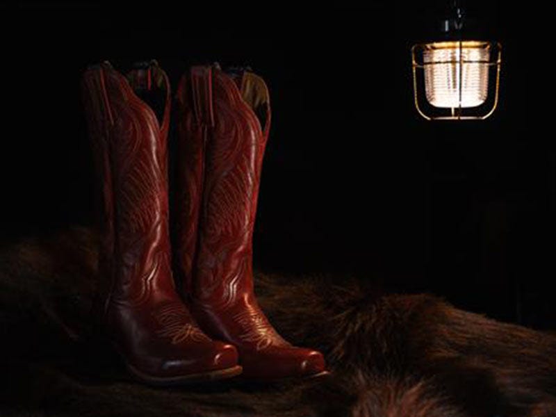 Red cowboy boots on a table illuminated by a lantern hanging above them.