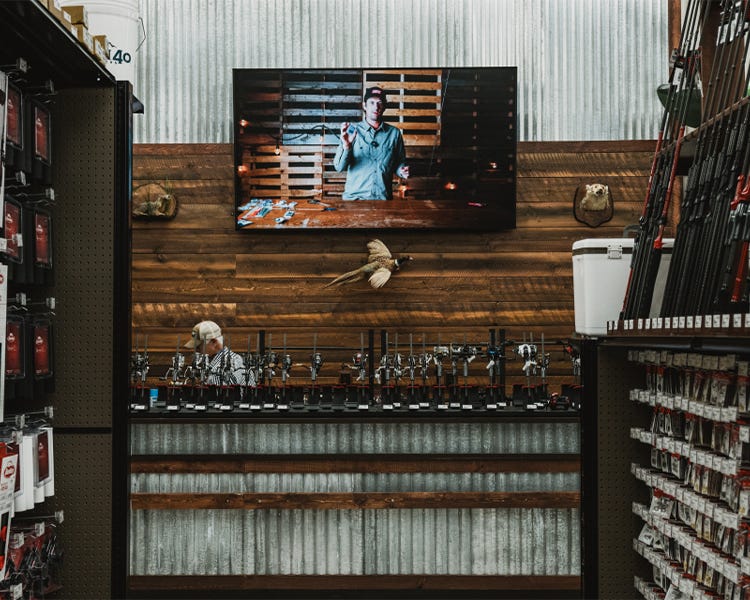 Fishing section at North 40 Outfitters Trent Spokane location. Fishing video playing on the tv in the background with rods and reels on display