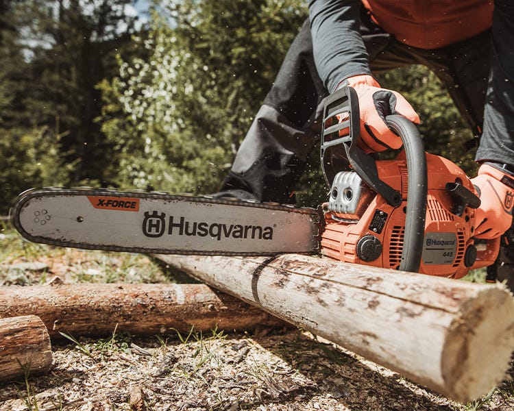 A man cuts a section of tree with a Husqvarna chainsaw