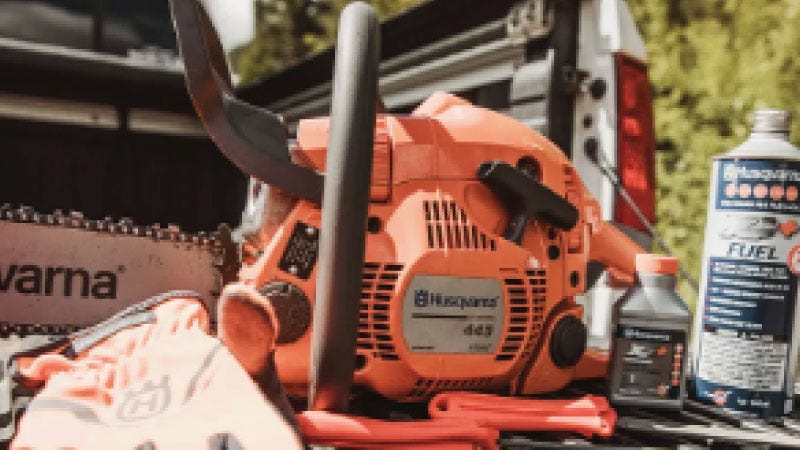 A Husquvarna chainsaw sitting on the back of a truck tailgate next to fuel and oil