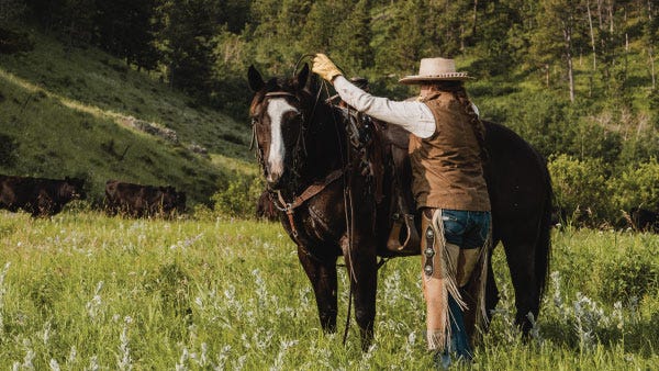 A cowgirl wearing Noble Outfitters goat skin gloves prepares to mount a horse