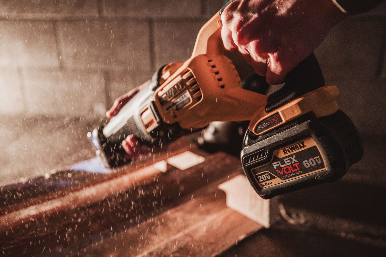A DeWalt FlexVolt reciprocating saw cuts into a piece of wood. Dust is kicked up into the sunlight.